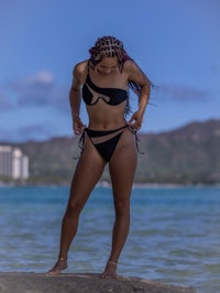 a woman in a black bikini standing on a rock